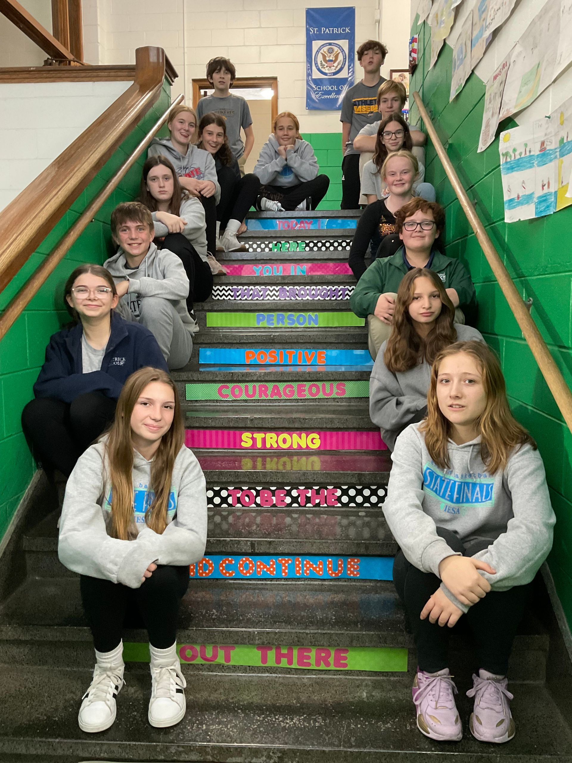 Group of students posing on colorful school stairs with inspirational words.