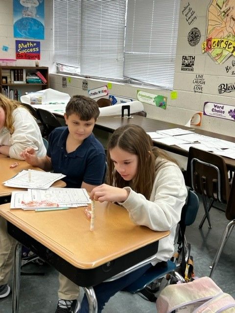 Students in classroom work on project, one boy and girl focused.
