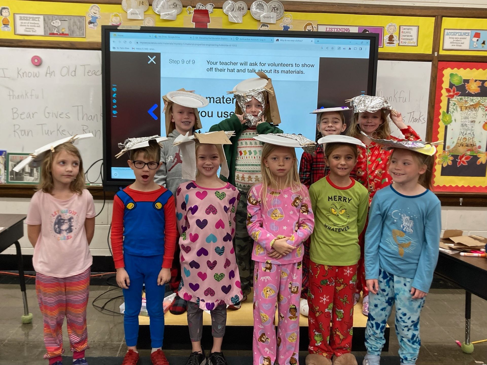 Children in pajamas wearing foil hats, in a classroom, posing for a photo.
