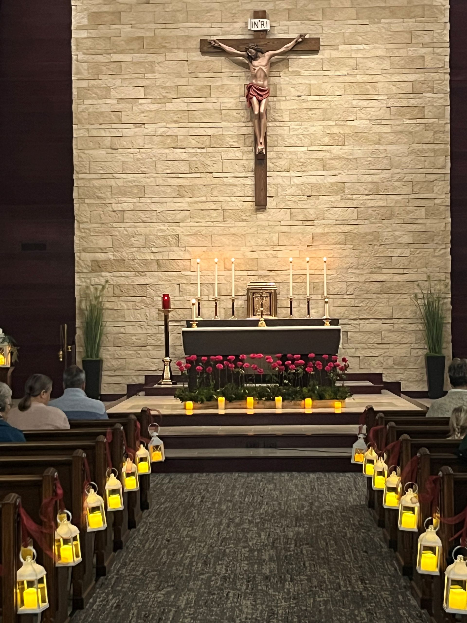 Church altar with cross, candles, flowers, and rows of pews decorated with lanterns.