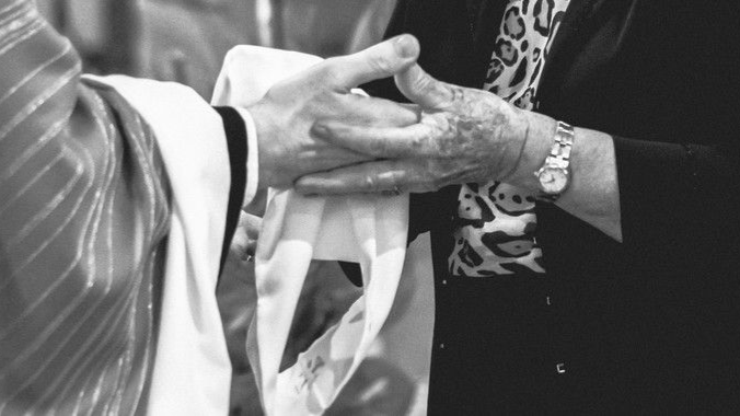Hands clasped in prayer; a priest holding a white cloth, blessing another.