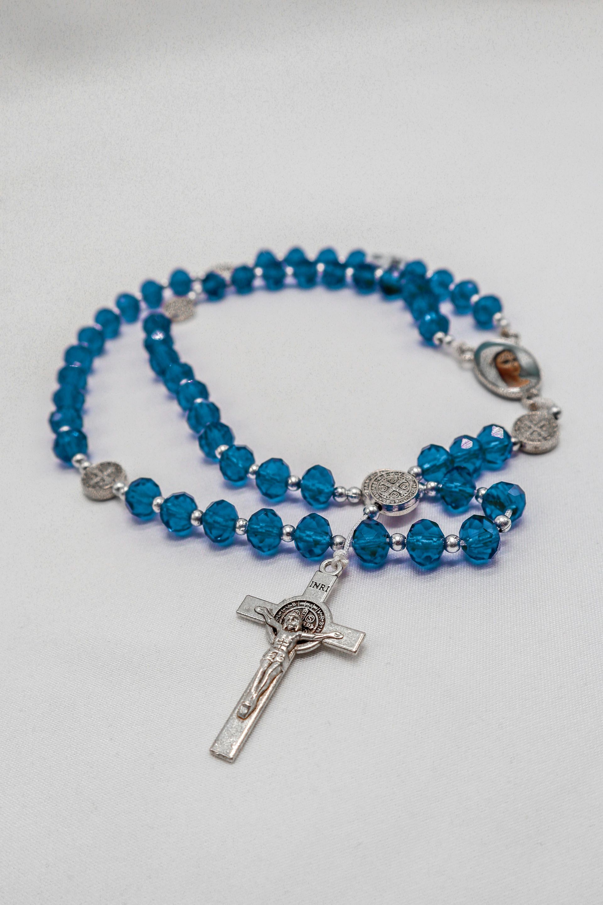 Blue beaded rosary with a silver crucifix and religious medallions on a white surface.