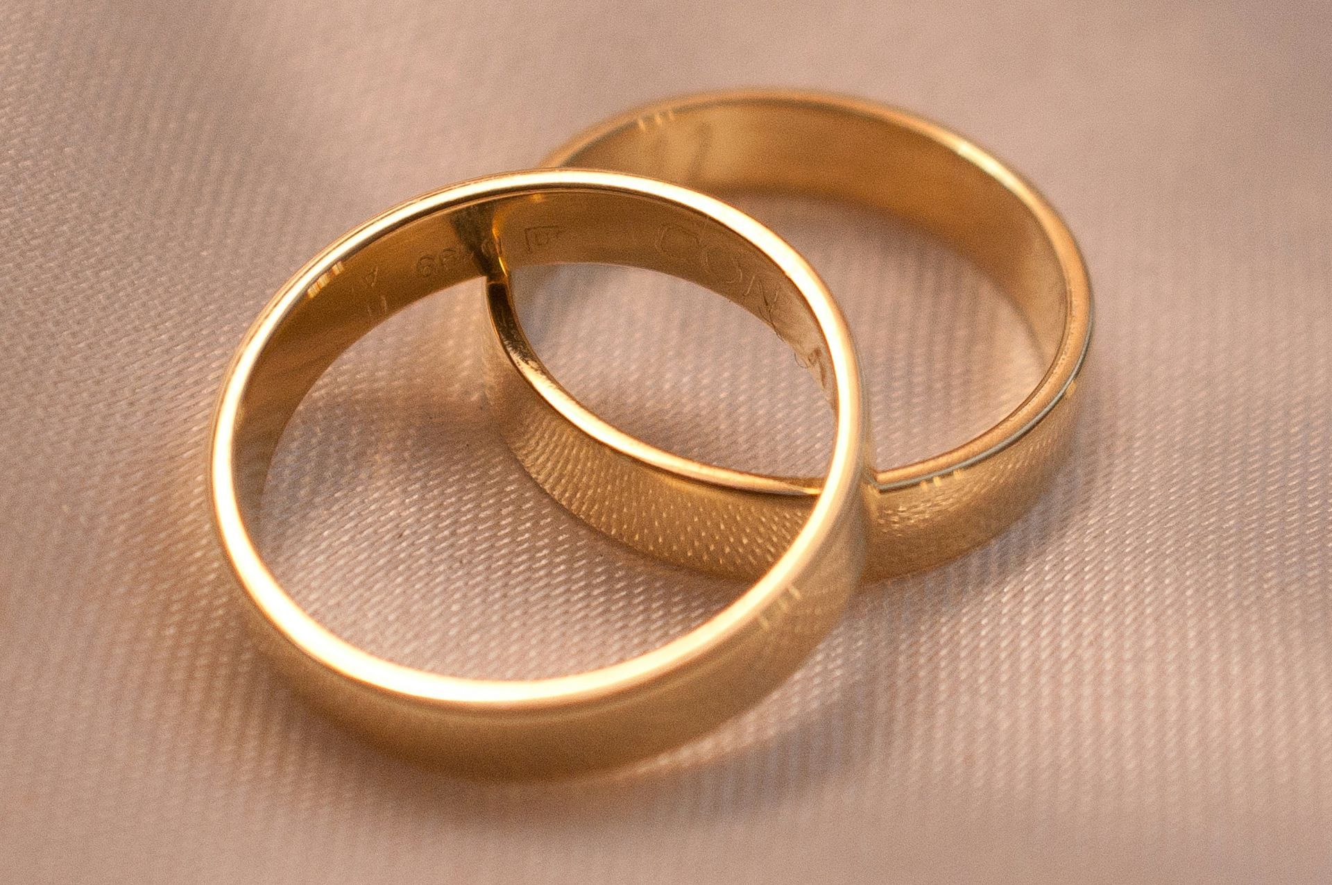 Two gold wedding rings on a cream-colored, slightly wrinkled surface.