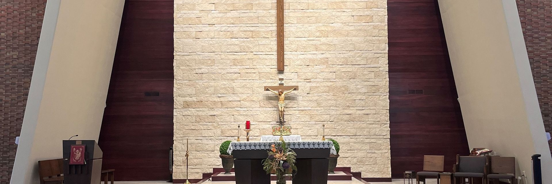Interior of a church with an altar, cross, and decorations.  Neutral wall with burgundy and brick sides.