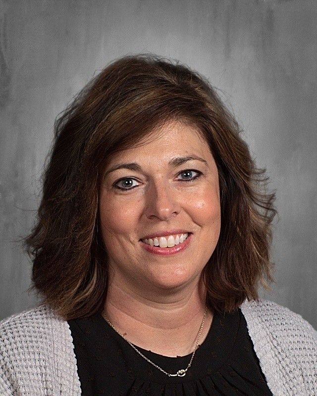 Woman with brown hair, smiling, wearing black top, white cardigan.