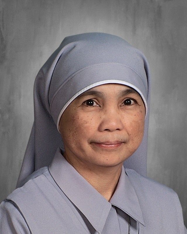 Smiling nun in a grey habit and veil, looking at the camera.