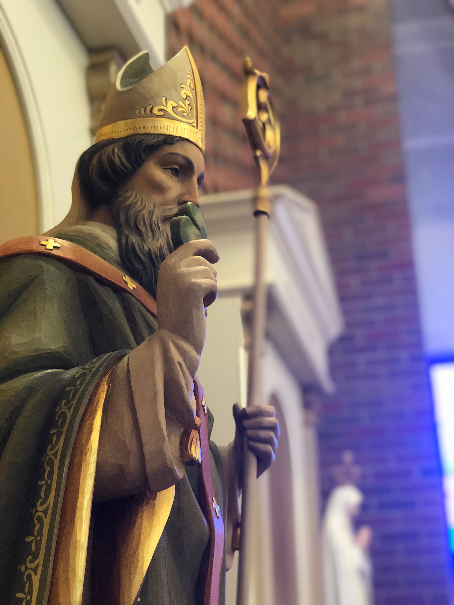 Statue of a bishop in green and gold robes, holding a staff, inside a church.