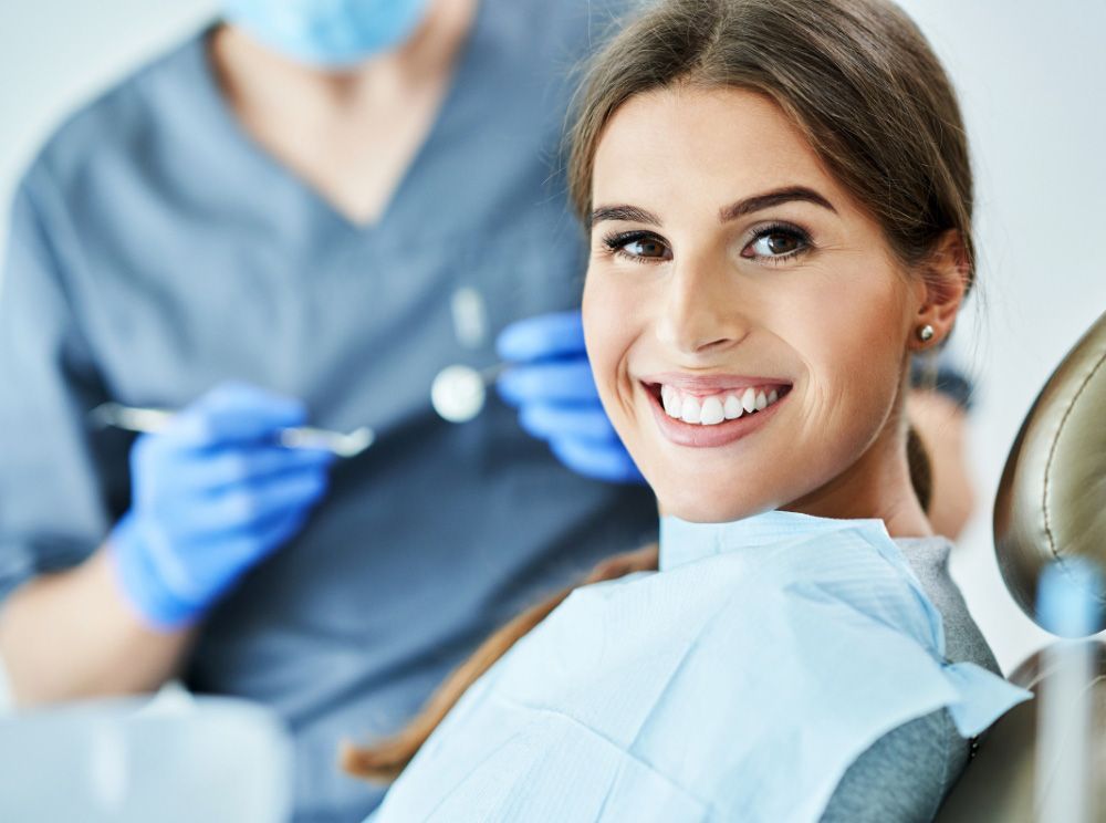 Woman smiling at dentist, dental tools in background, blue gloves.