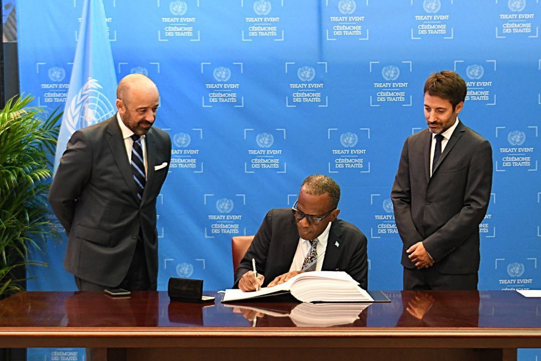 A man in a suit is signing a document while two other men look on.