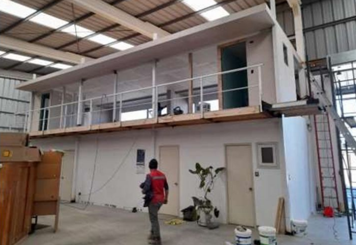 Un hombre con una chaqueta roja está parado frente a un edificio con balcón.