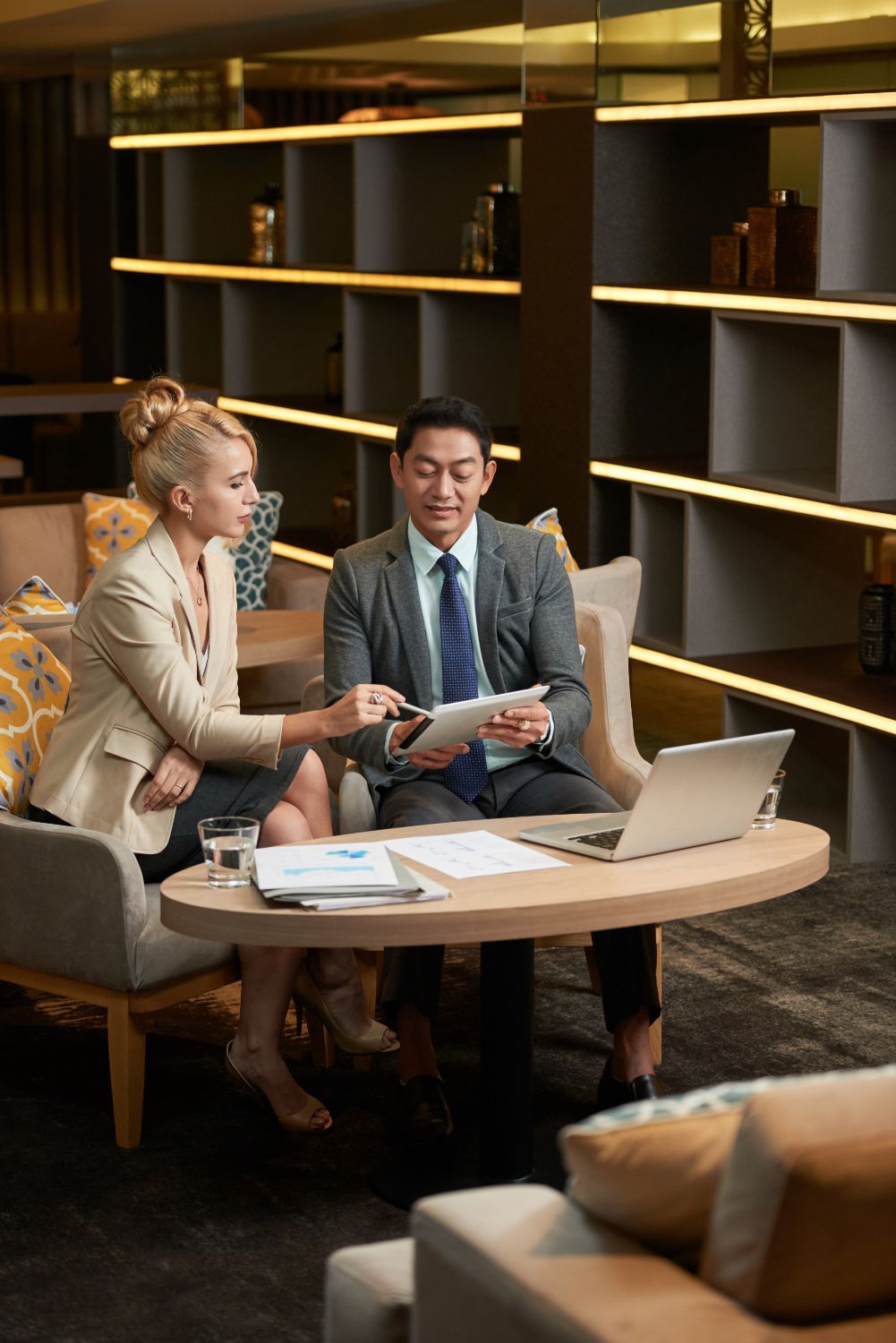 Two businesspeople reviewing documents at a table in a modern lounge setting.