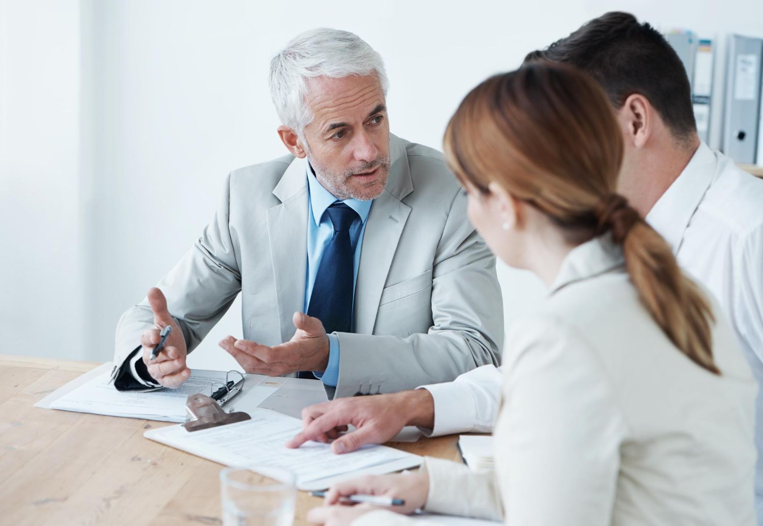Man in suit gestures, discussing documents with two colleagues at a table.