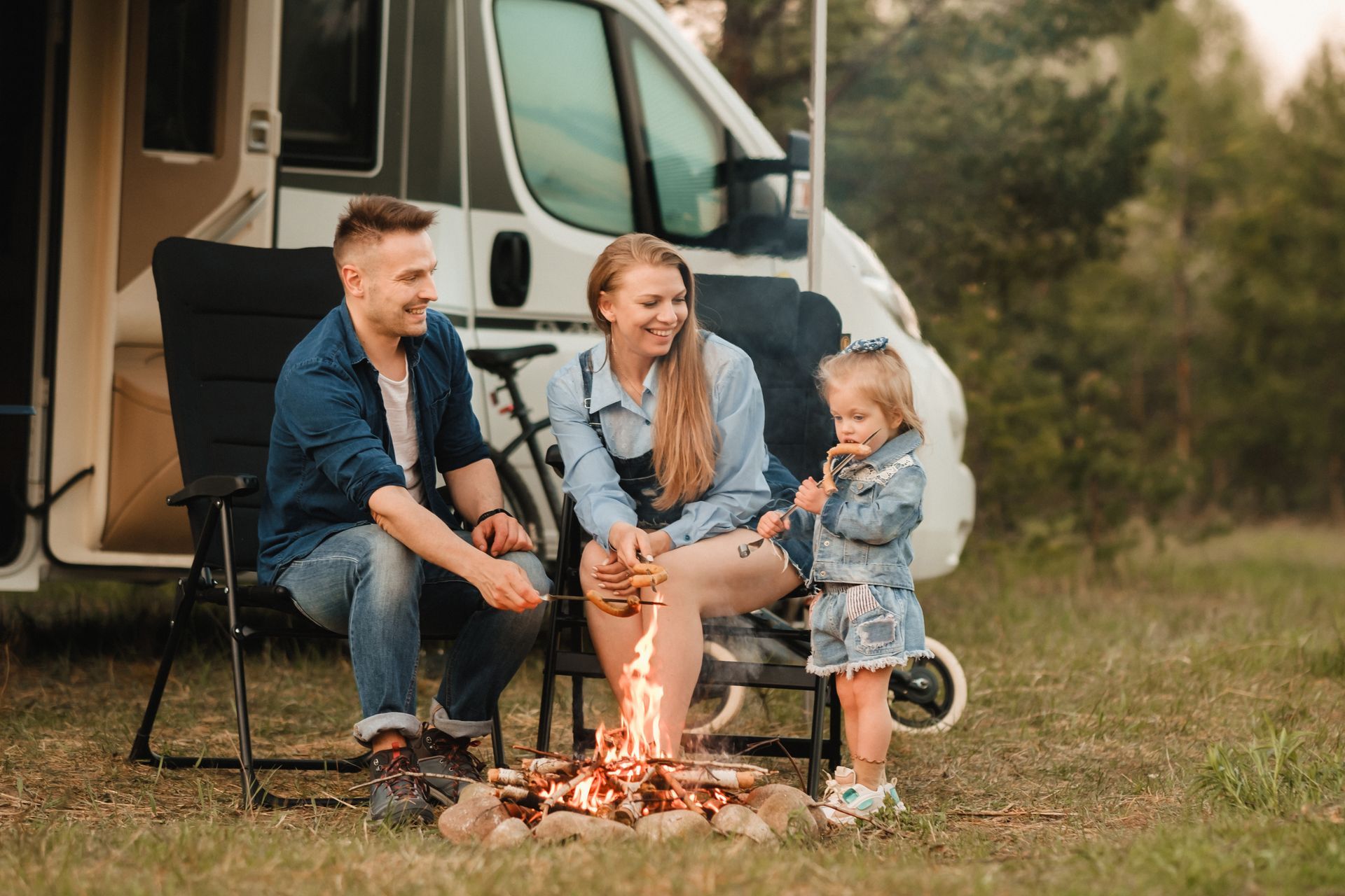 Family roasting marshmallows by a campfire near a camper van.