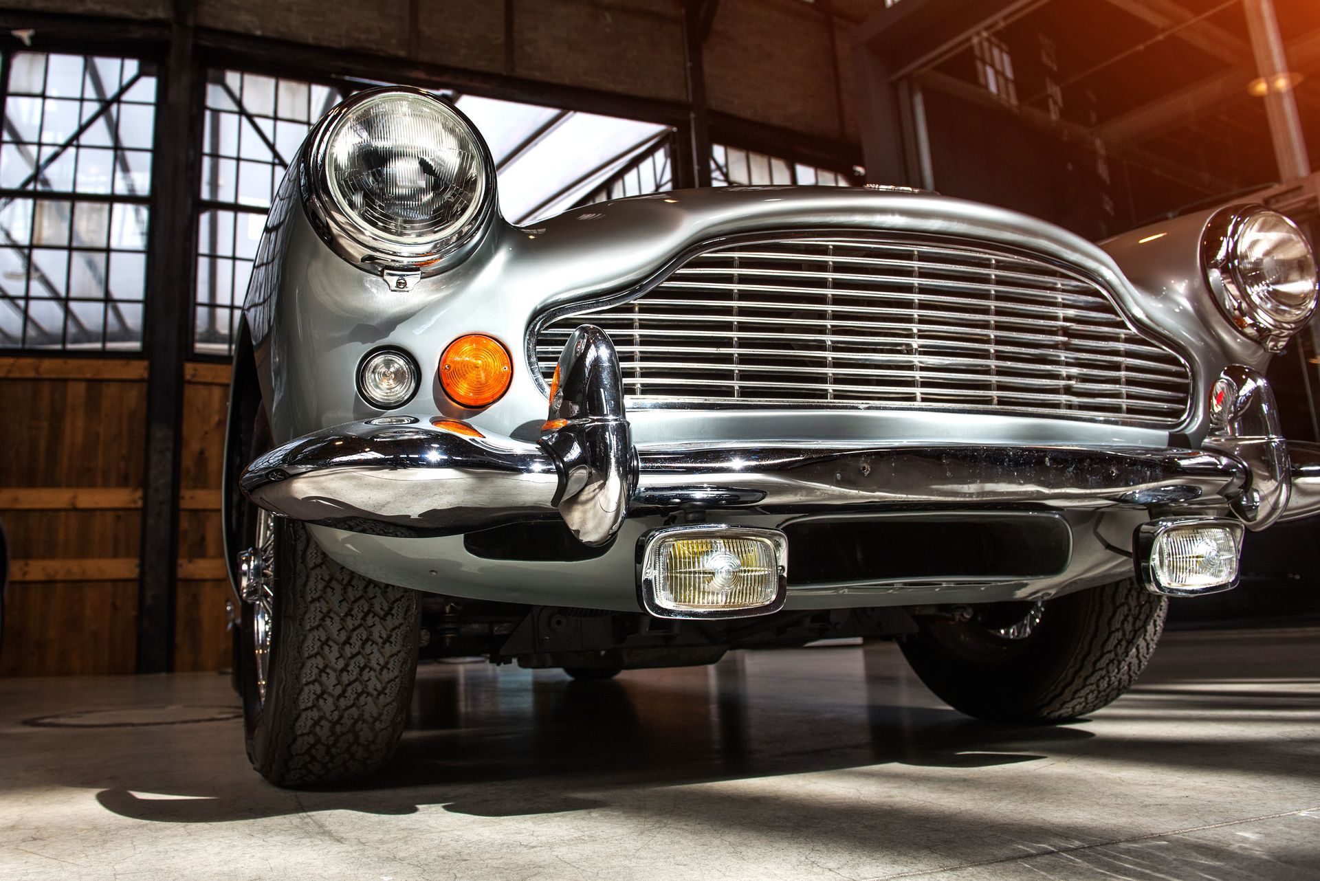 Silver classic Aston Martin DB5 car, front view, chrome details, orange indicator lights.
