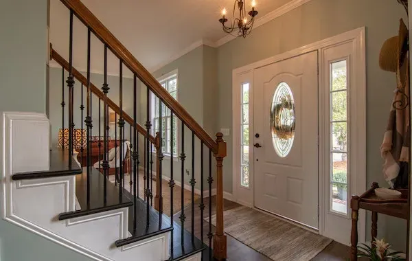 Entryway with staircase and front door; light blue walls, brown railing, white door with sidelights.