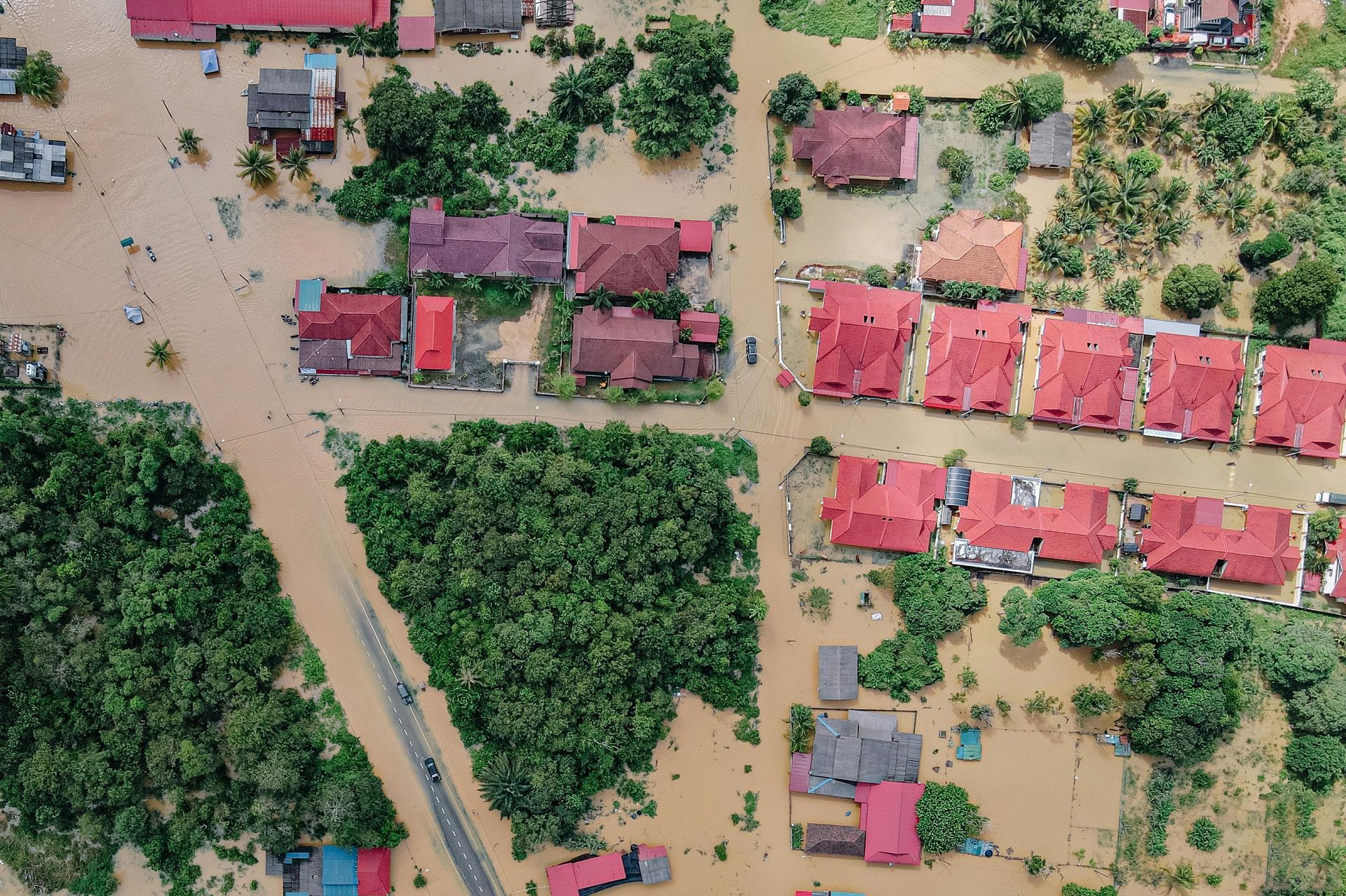 Aerial view of flooded houses in a neighborhood. Brown water surrounds red-roofed buildings and trees.