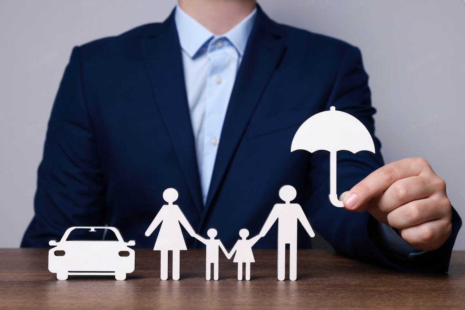 Man in suit holding umbrella cutout over family and car cutouts on a table.