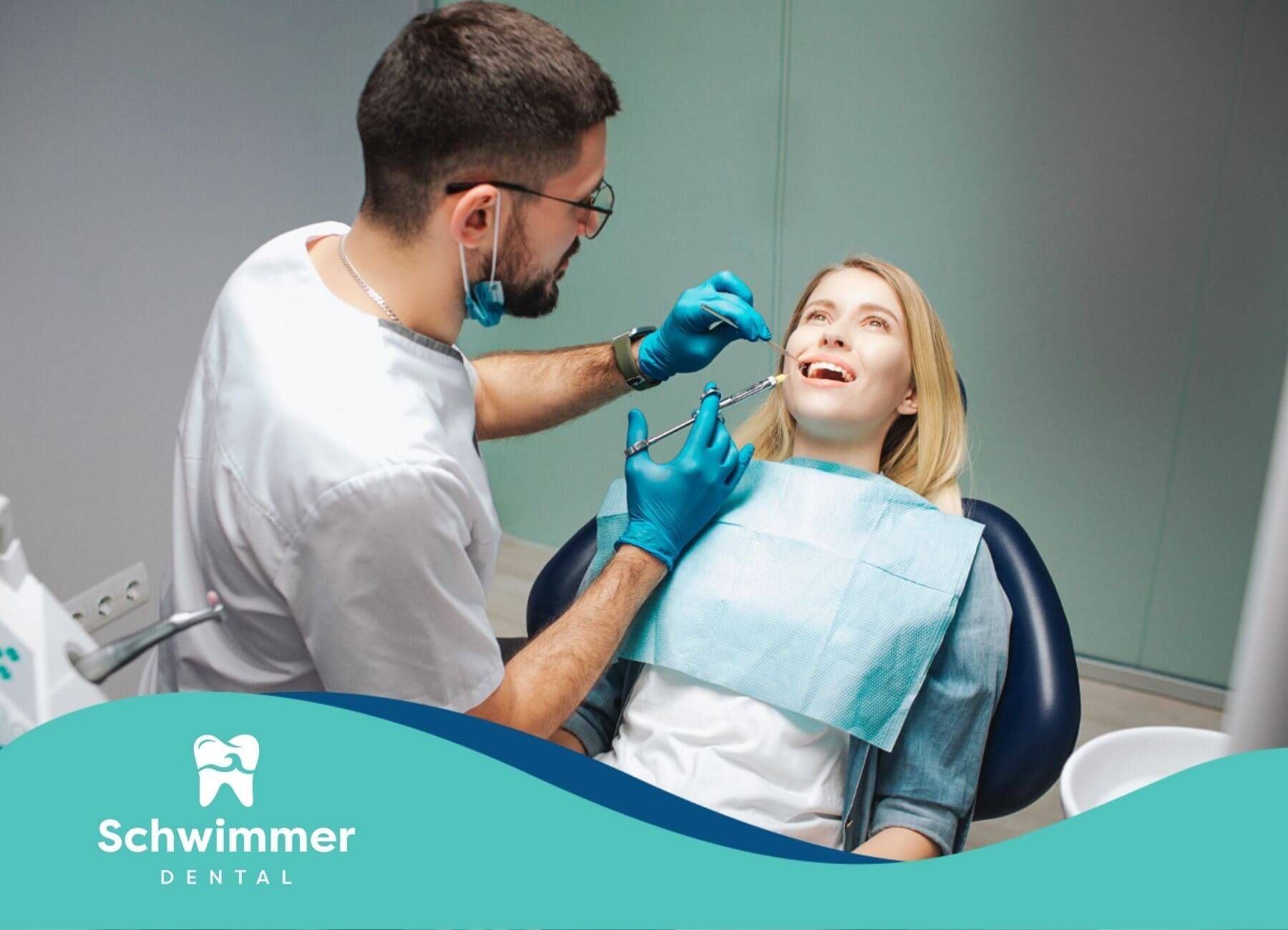 Dentist injecting patient's mouth with a syringe; blue gloves, light setting.