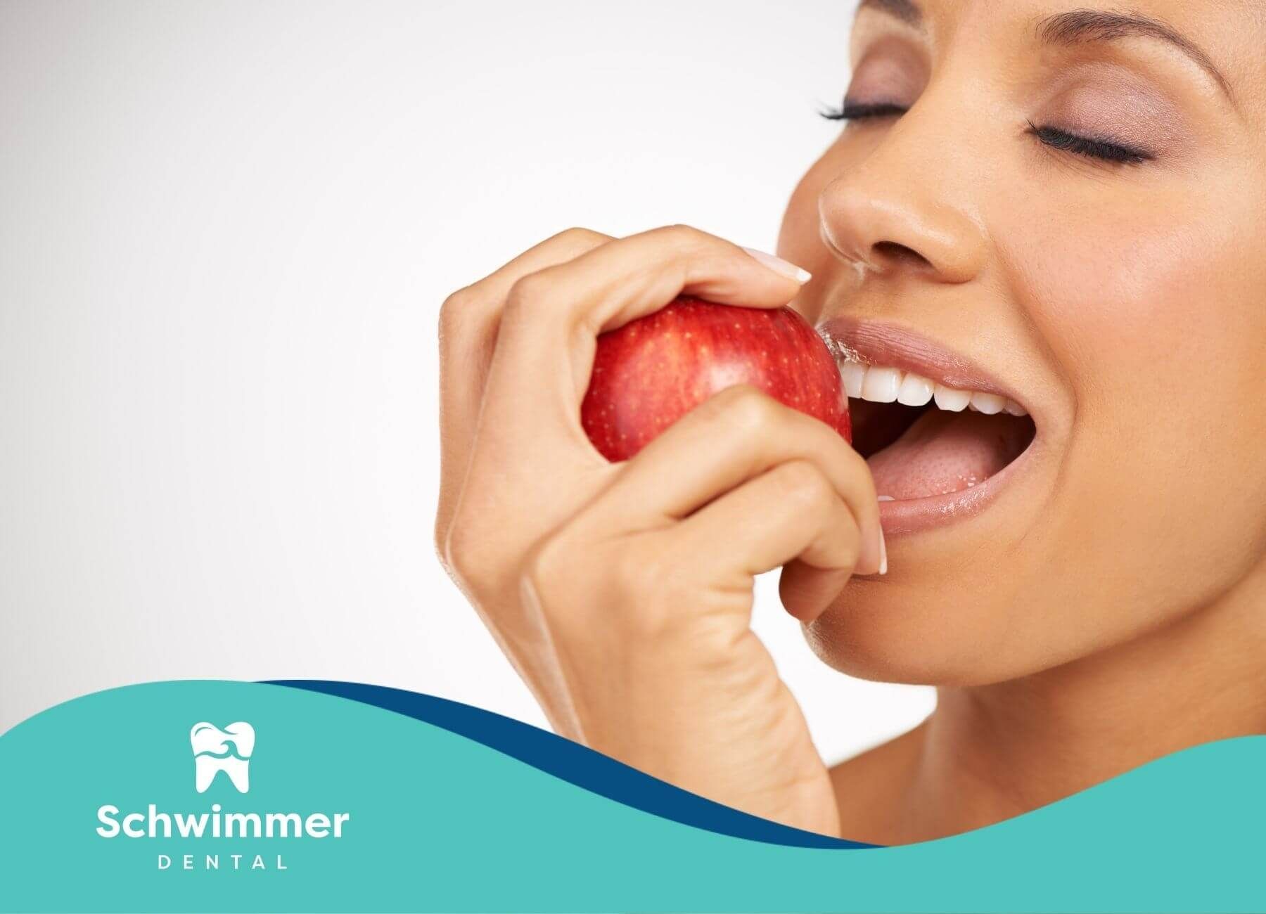 Woman biting into a red apple with healthy white teeth, demonstrating strength and function