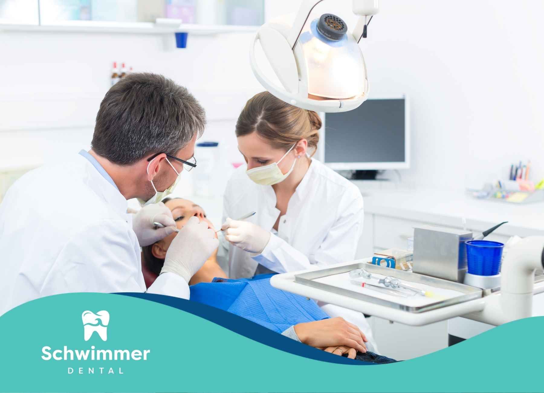 Dentist examining a patient's mouth, with an assistant present. Clinic setting, bright with dental tools.