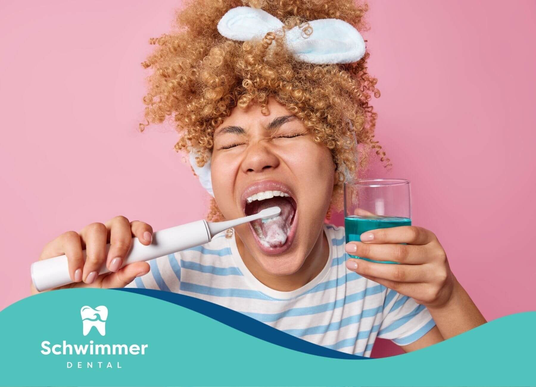 Woman with curly hair screams while brushing her teeth with an electric toothbrush, holding a glass.