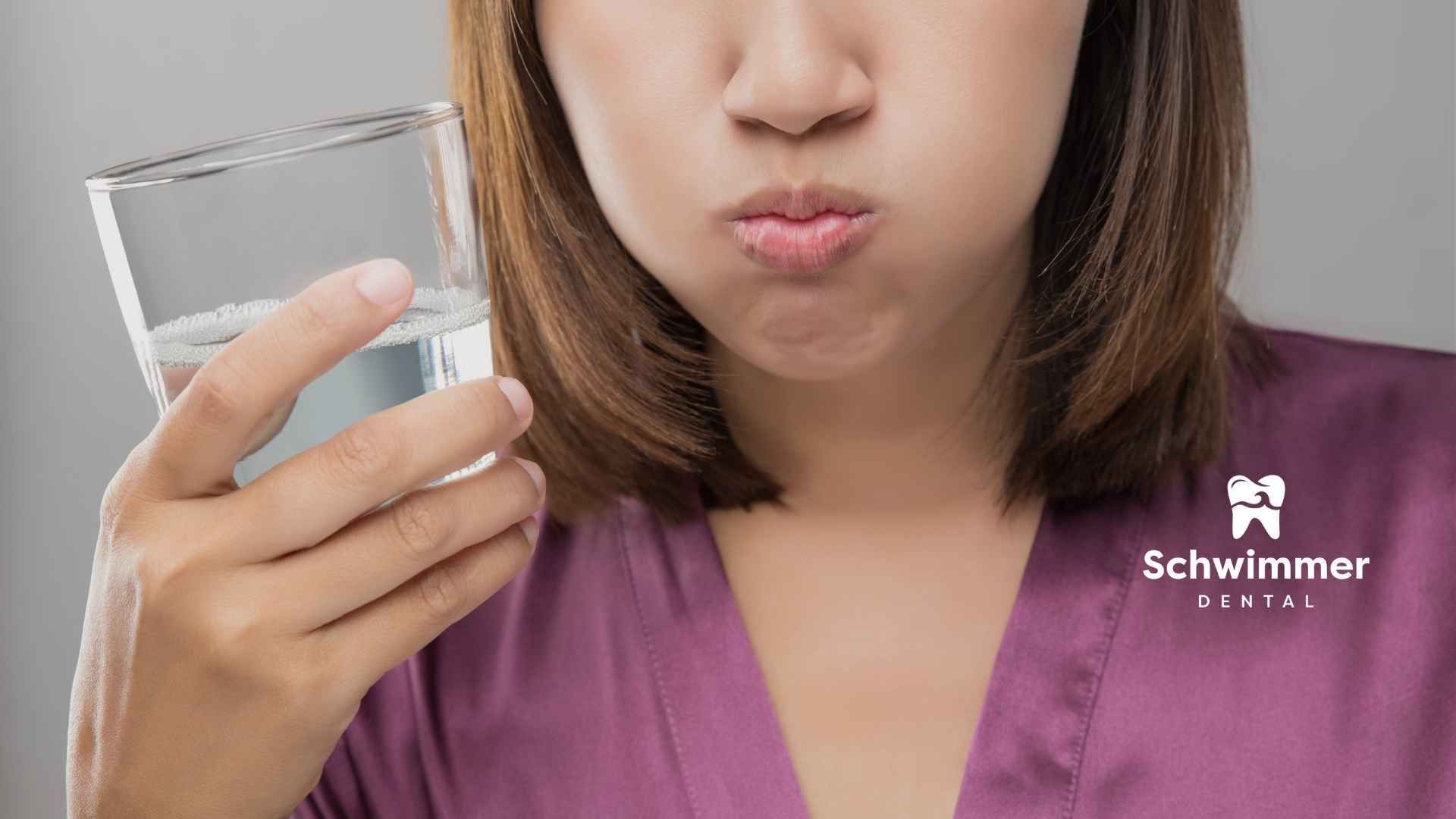 A woman is holding a glass of water in front of her mouth.