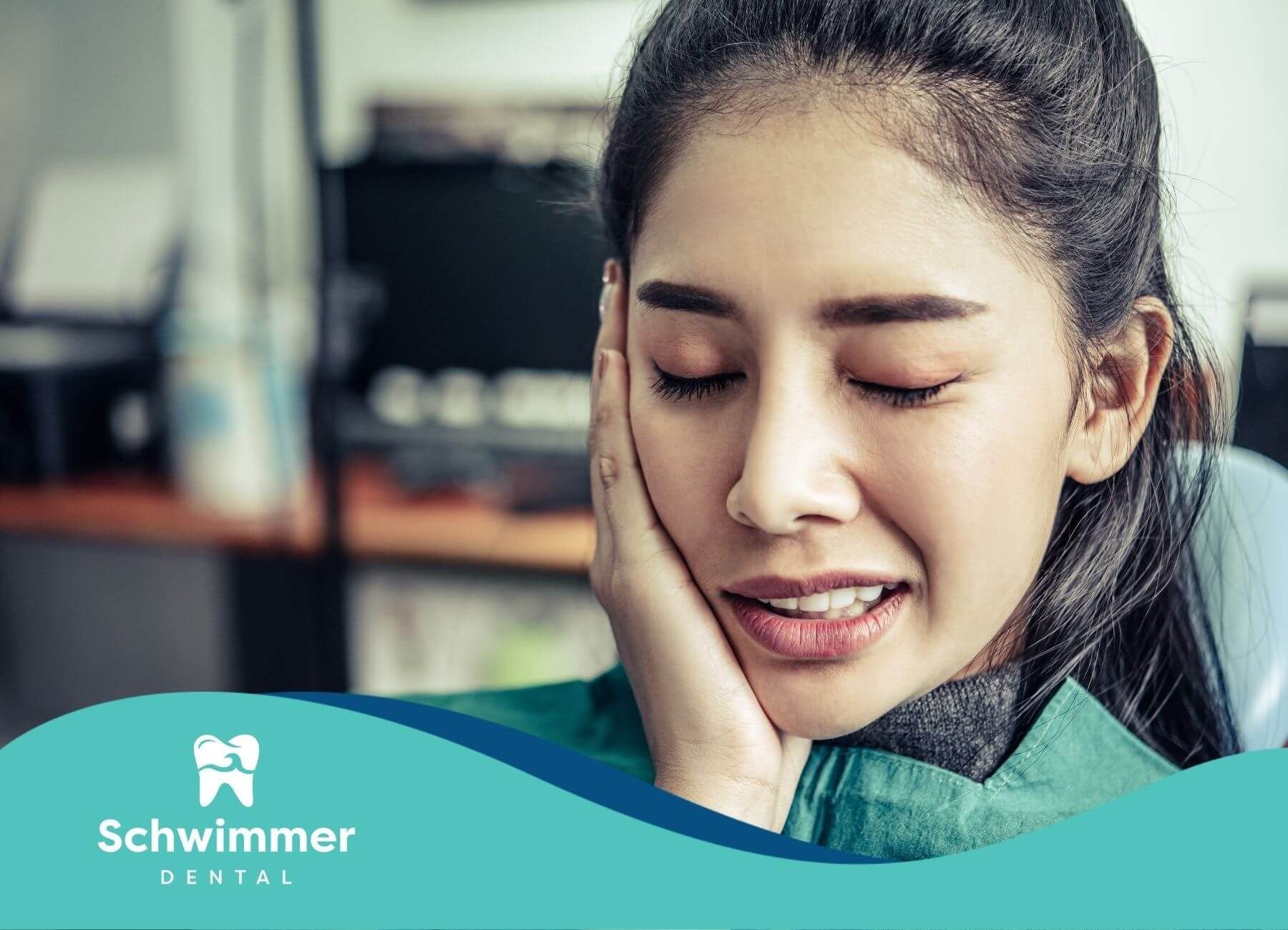 A woman showing discomfort with her hand on her jaw while sitting in a dental chair during treatment