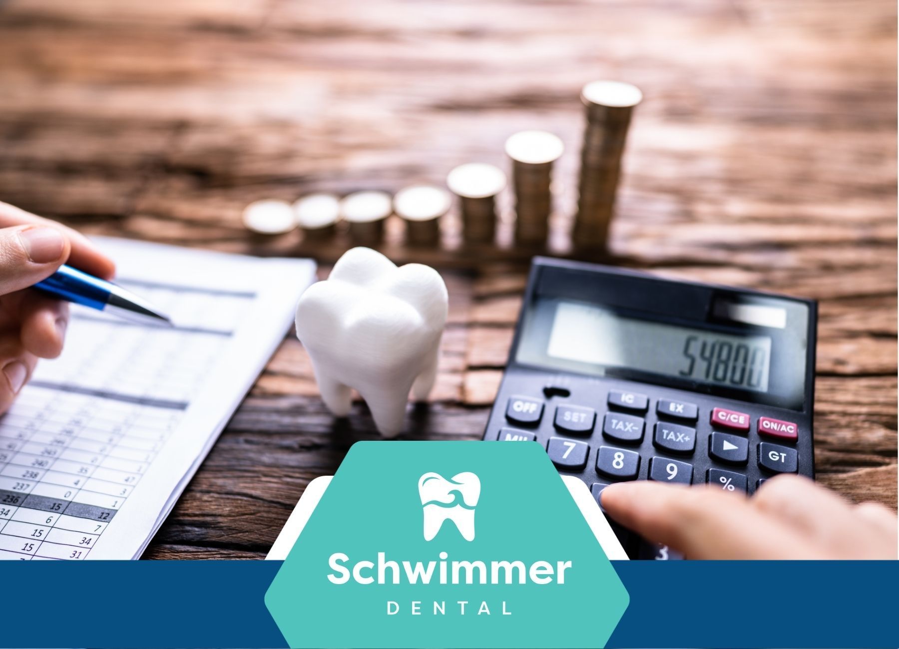 A person is using a calculator next to a tooth and coins.