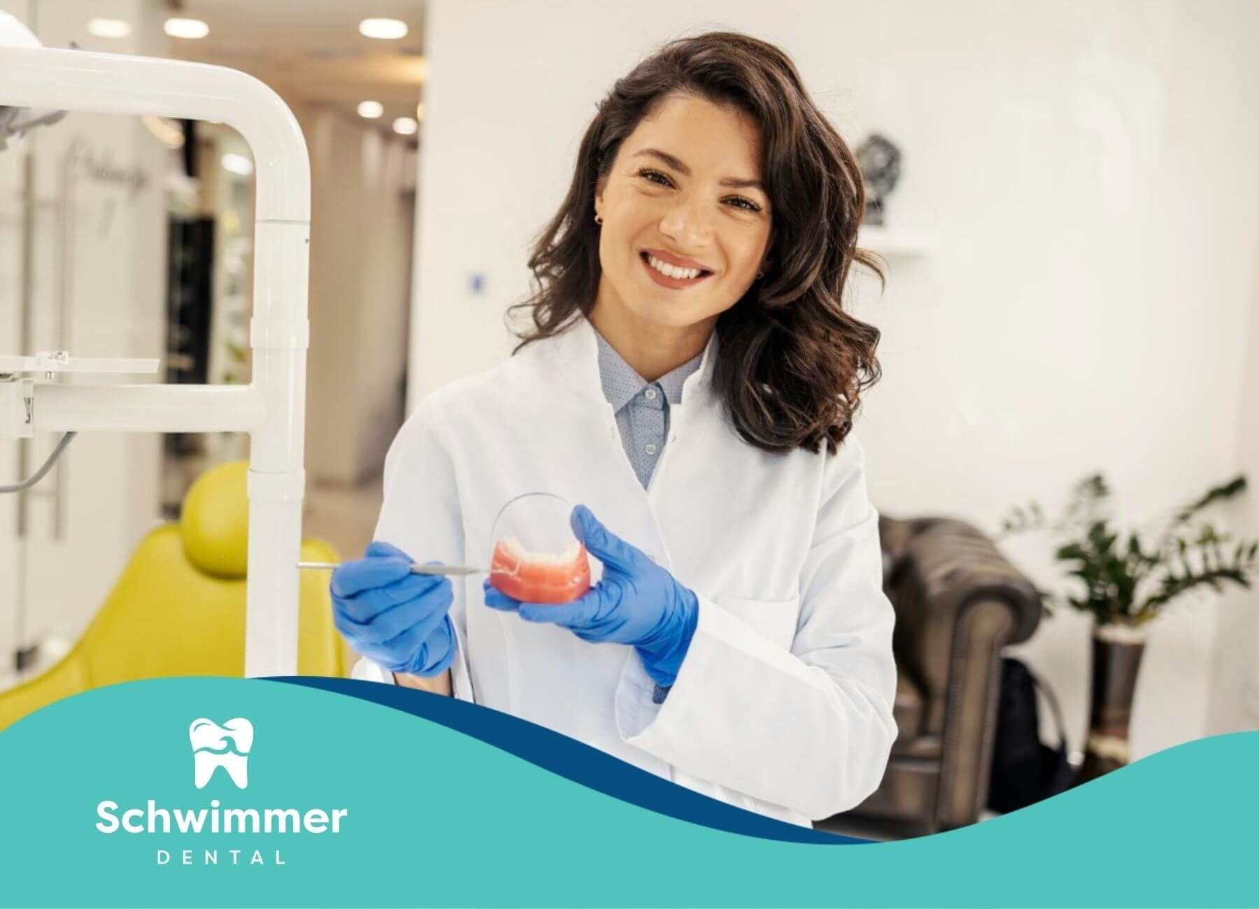 Smiling dentist holding a dental model in a clinic.
