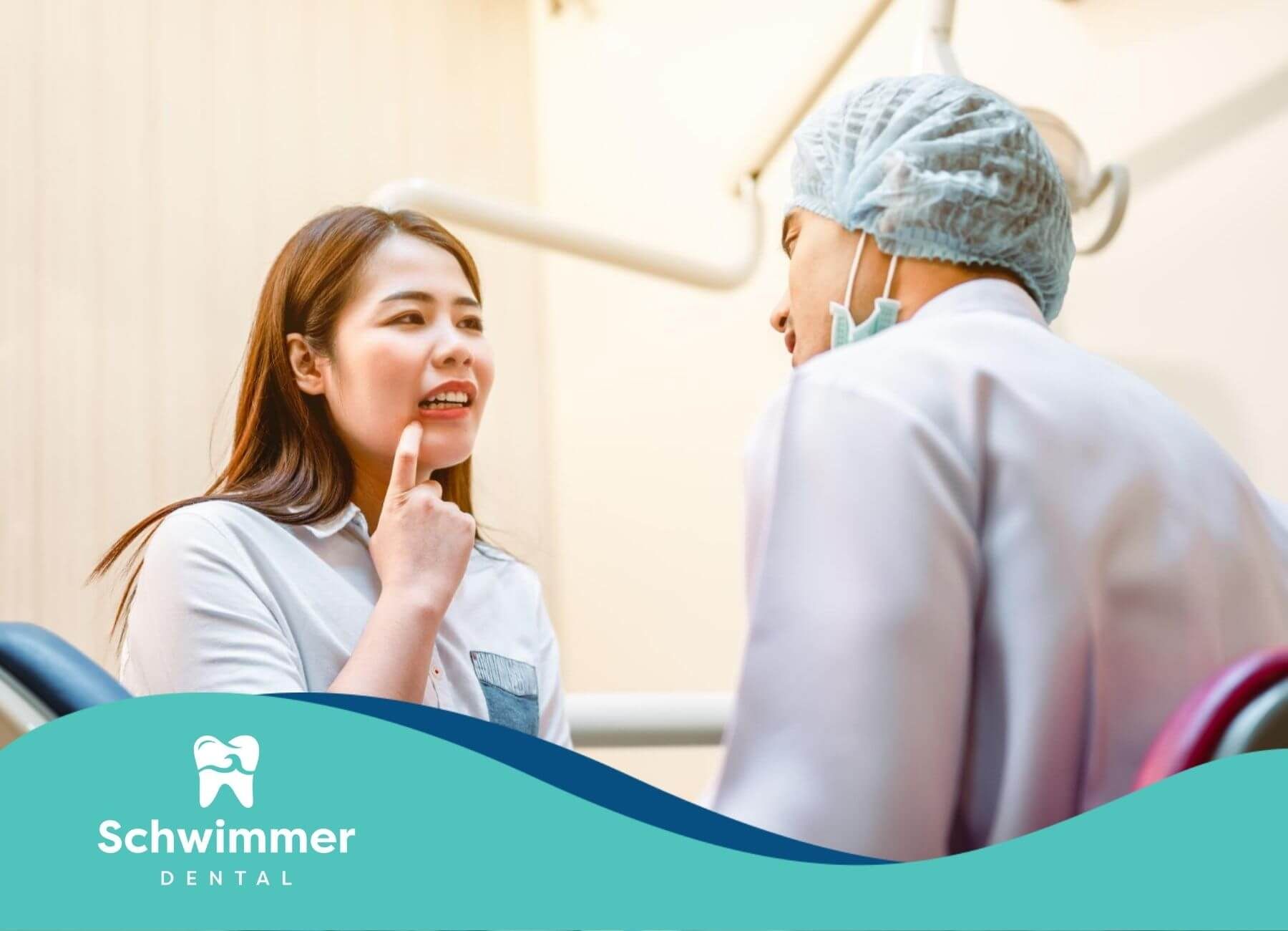 A woman points to her mouth while talking to a dentist in a dental office.