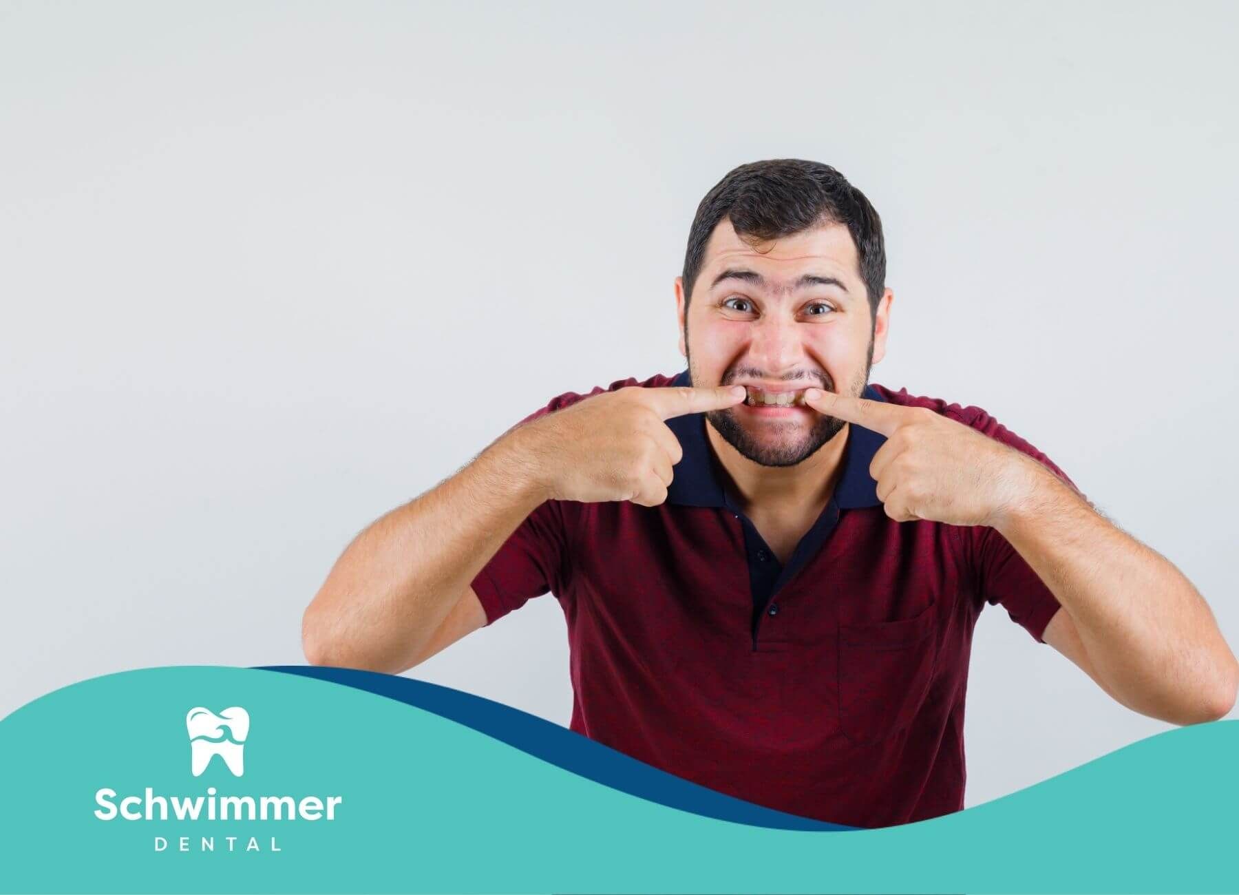 A man making a forced smile with his fingers, showing his teeth, against a plain background.
