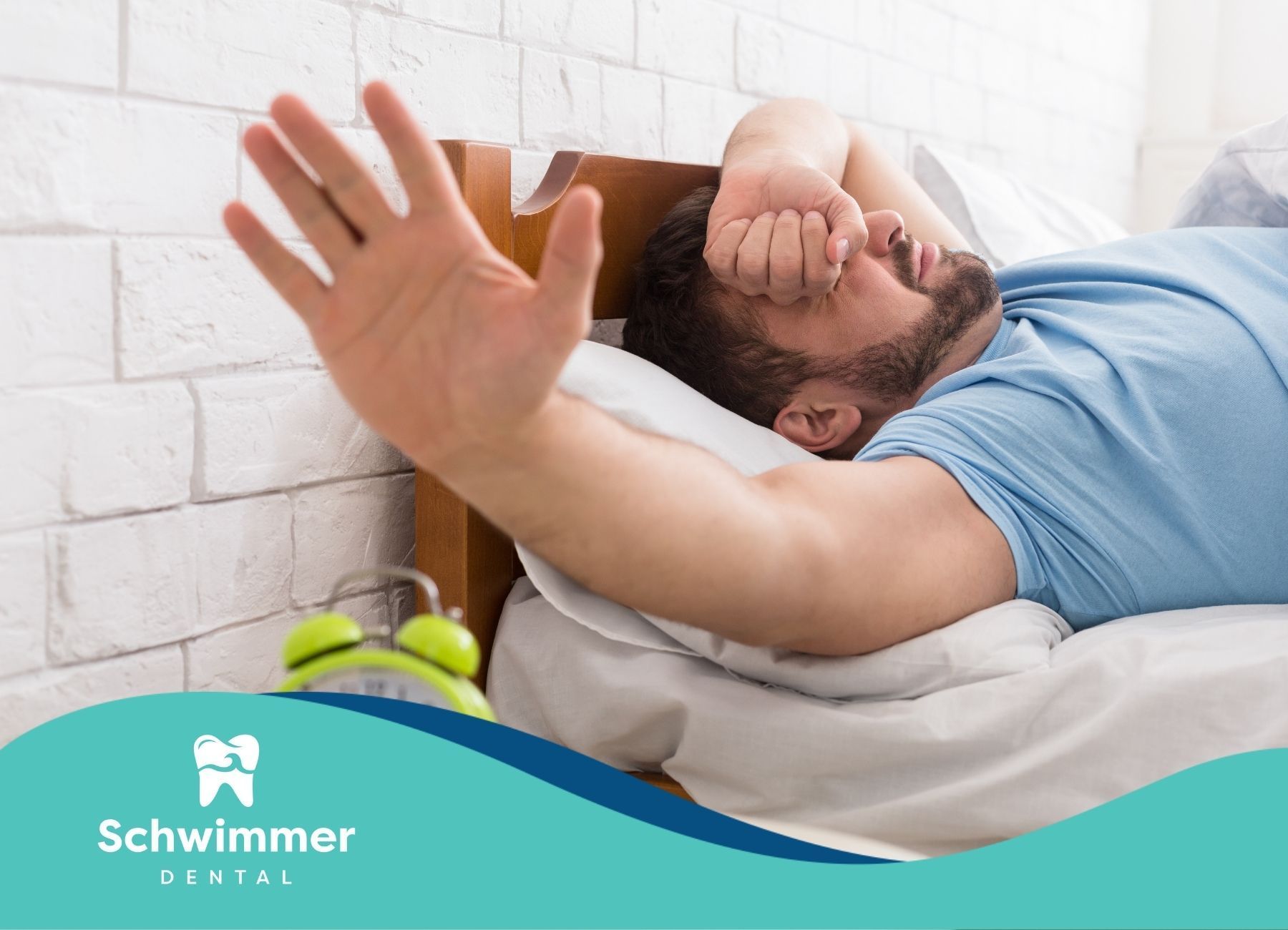 Man in bed, reaching for alarm clock, covering eyes; light green clock on nightstand.