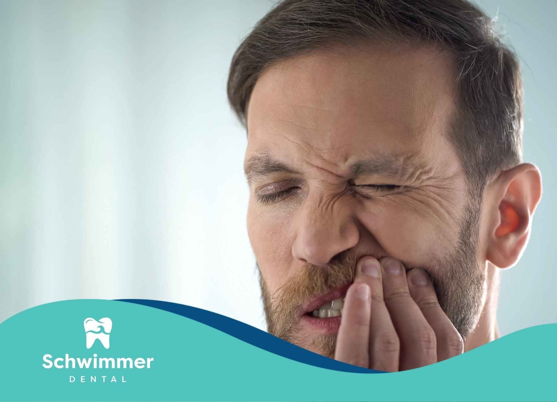 A man with a beard is holding his mouth in pain.