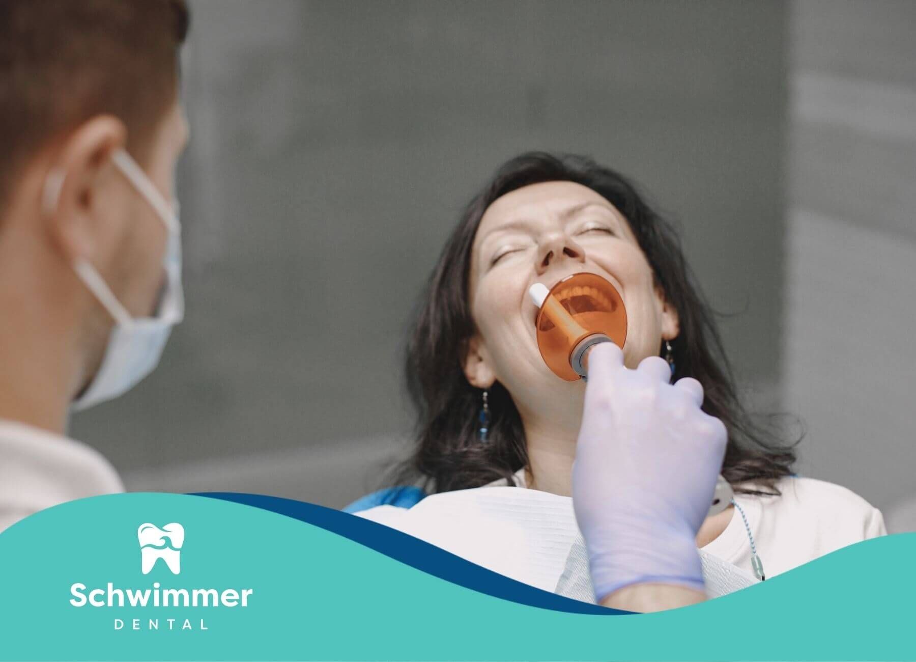 Dentist using an orange curing light during a dental procedure while patient reclines comfortably.
