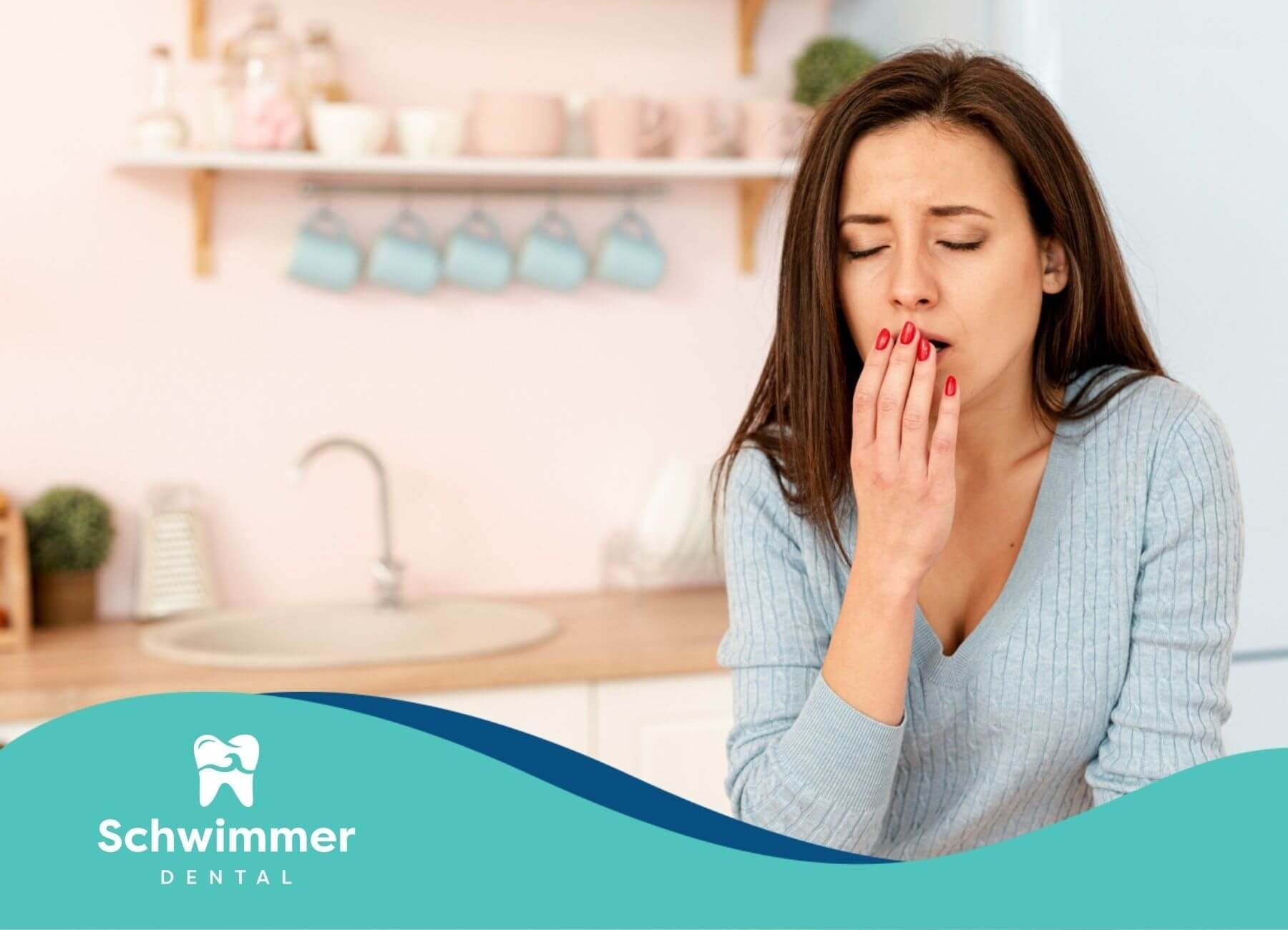 Woman covering mouth due to tooth pain in kitchen.