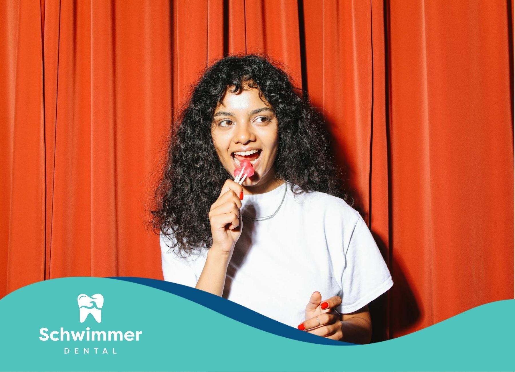 Woman smiling while eating a red and sweet lollipop in front of a red curtain in Point Pleasant, NJ.