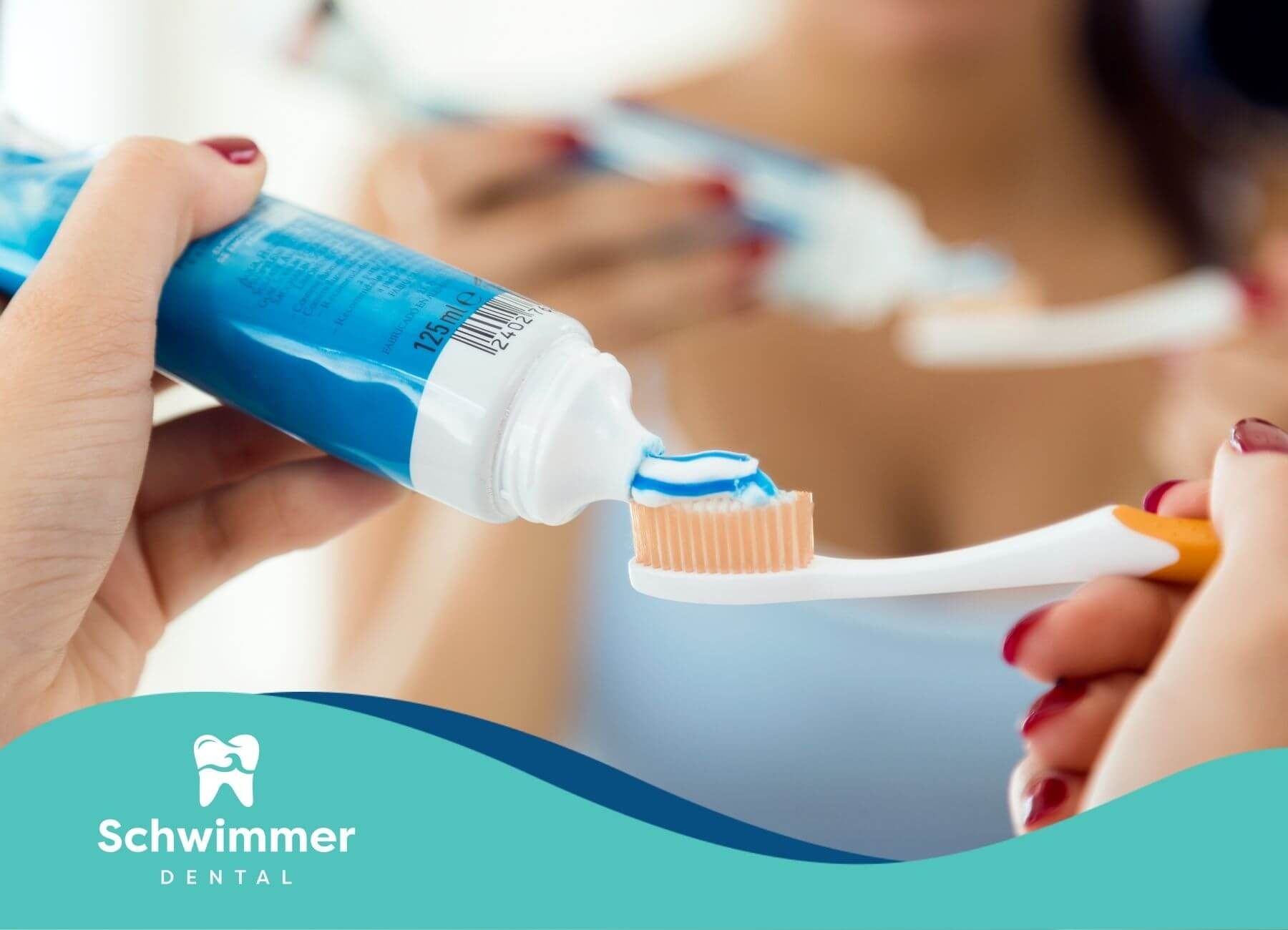 A close-up image of someone applying toothpaste to a toothbrush with blue and white toothpaste