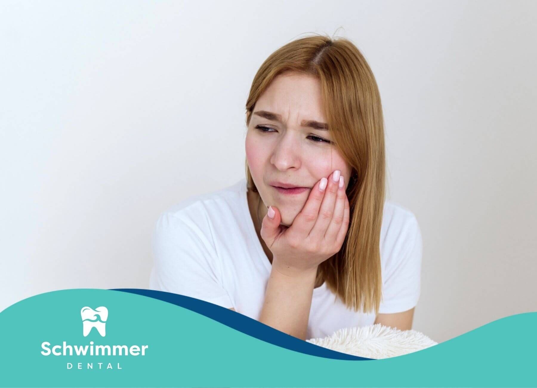 A woman is holding her mouth in pain while sitting on a bed.