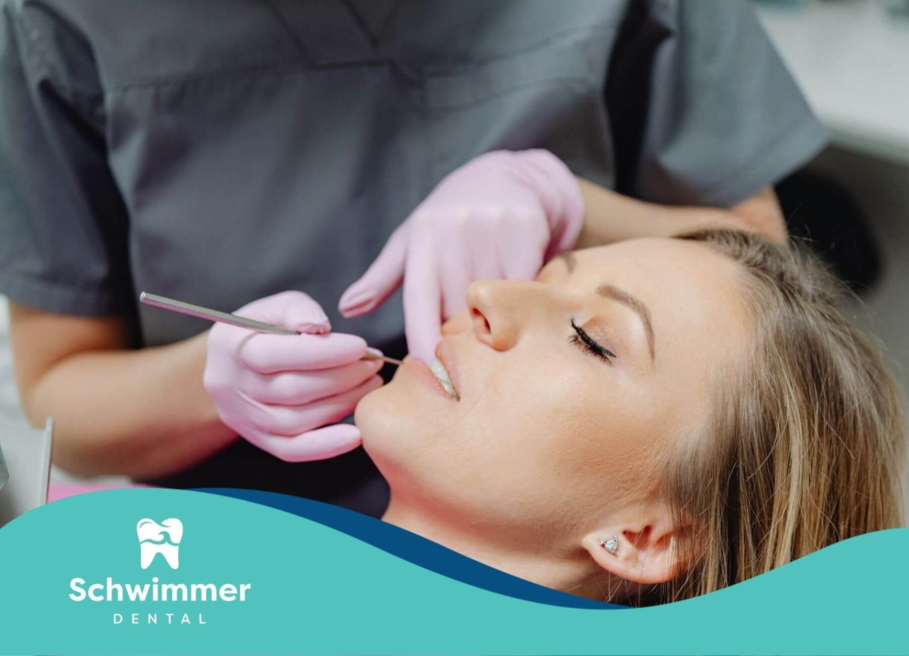 Dentist checking female patient’s teeth with dental tools and pink gloves.