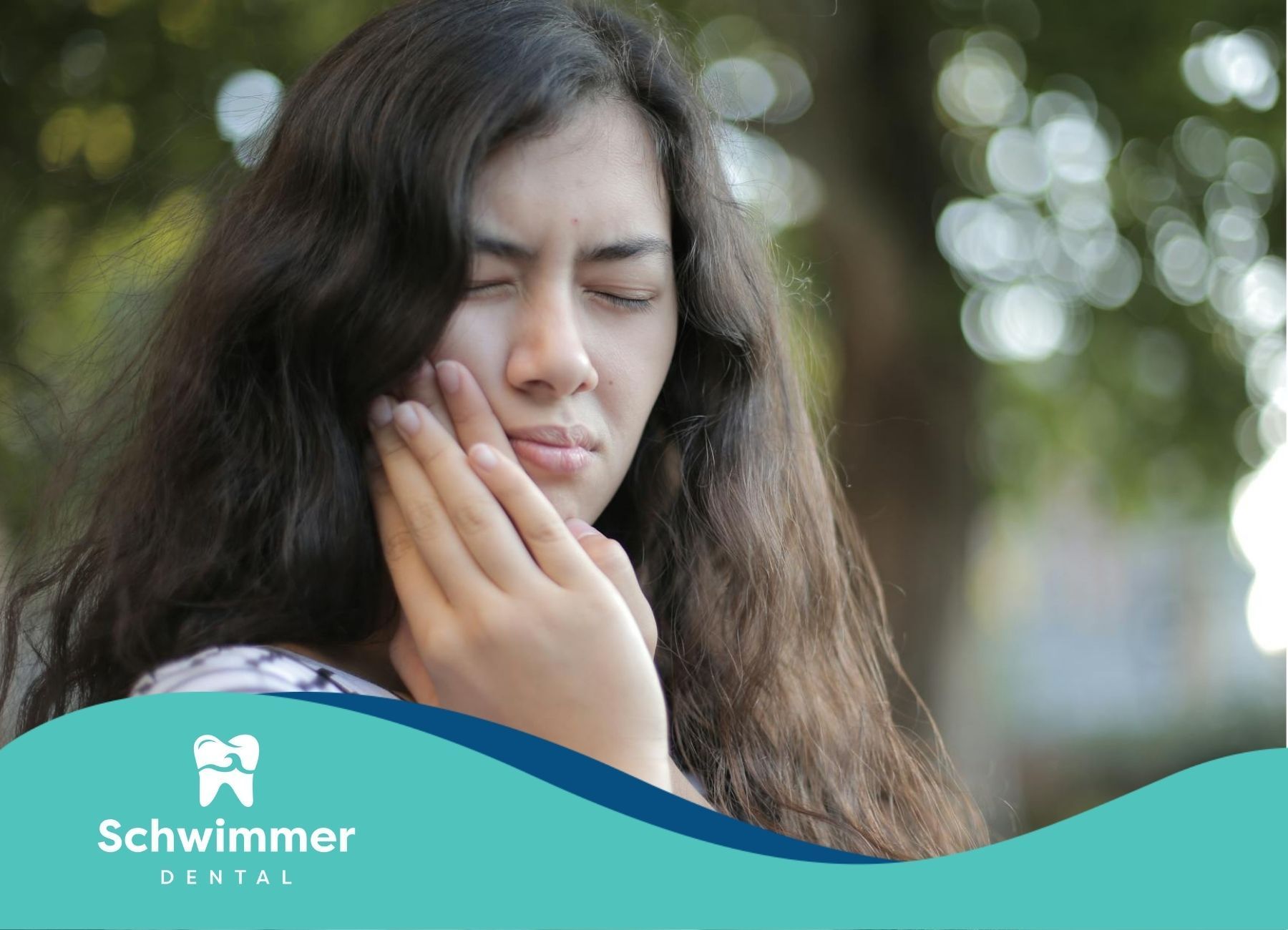 A young woman with long dark hair holds her cheek in pain, signaling dental emergency in NJ.