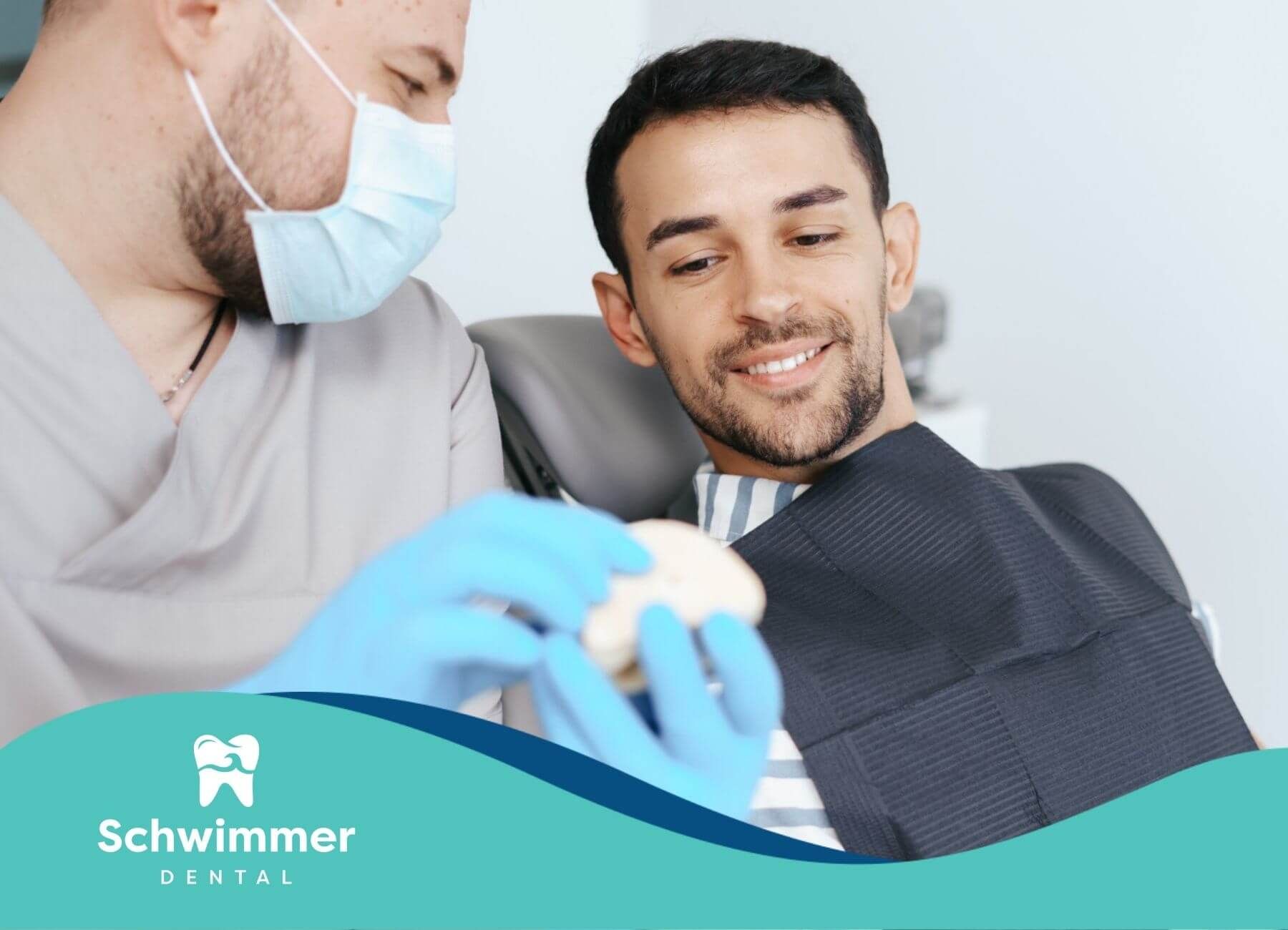 Dentist showing a dental model to a smiling male patient.