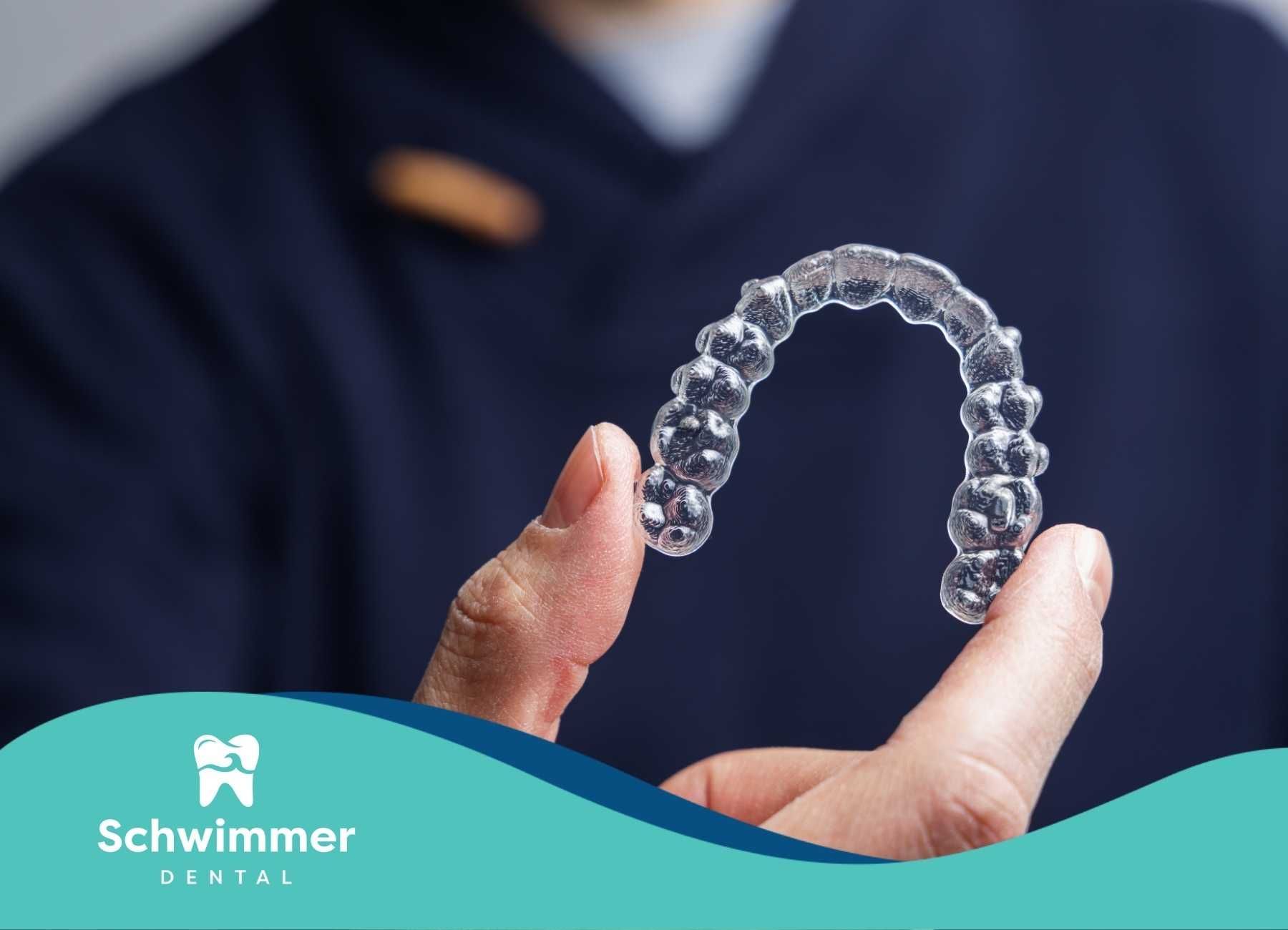 Hand holding clear dental aligner. Blue suit in background.
