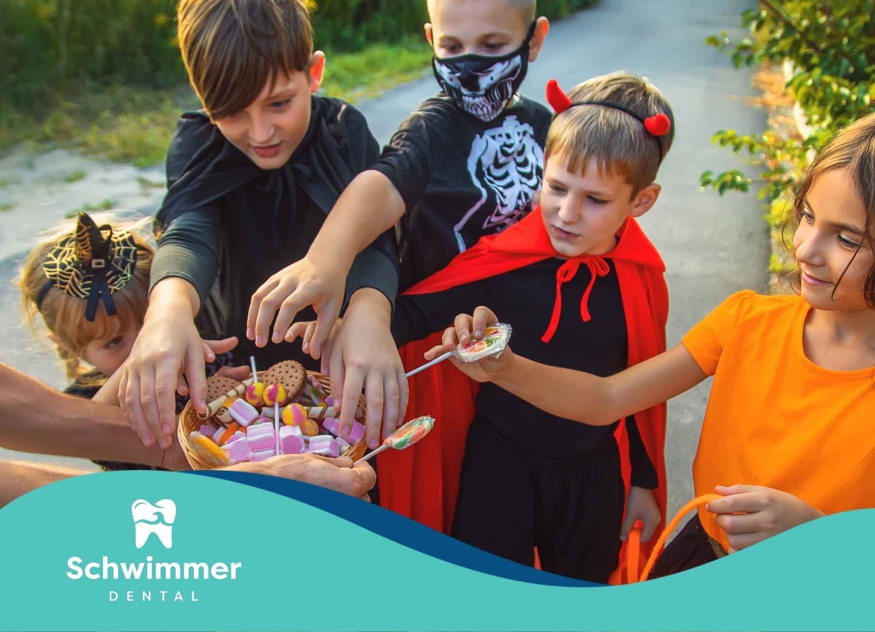 Children in Halloween costumes reaching for candy from a person's outstretched bucket outdoors.