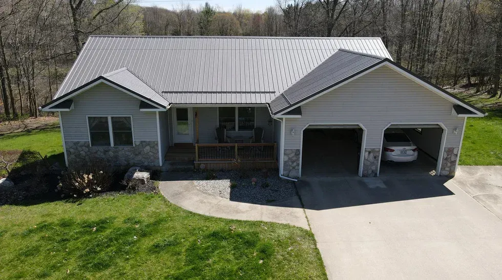 A gray house with a metal roof and attached garage; a car is parked inside.
