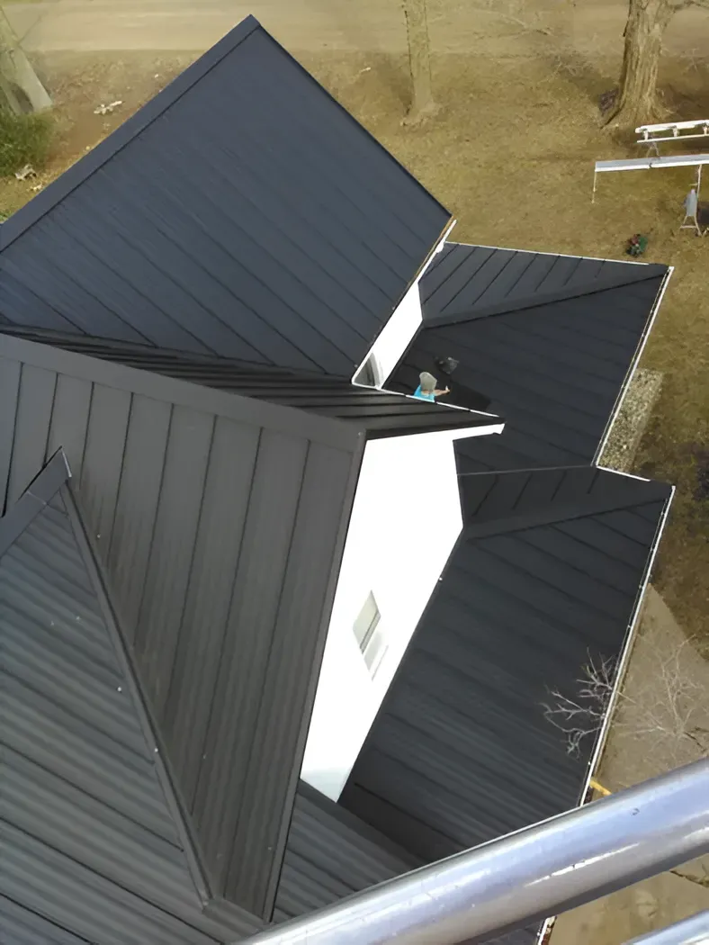 Black metal roof on a white building, viewed from above, with a silver railing in the foreground.