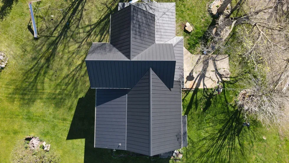 Overhead view of a house with a dark gray roof and surrounded by green grass and trees.