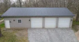 Tan three-car garage with white doors and dark gray roof. Concrete driveway.