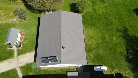 Overhead view of a house with a gray roof, solar panels, and a shed on a grassy property.