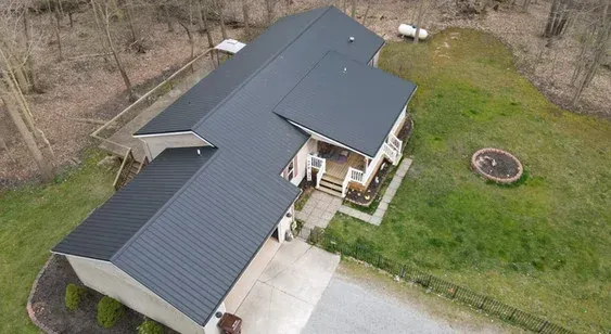 Black-roofed house on a hill, surrounded by greenery, with a porch and a stone fire pit.