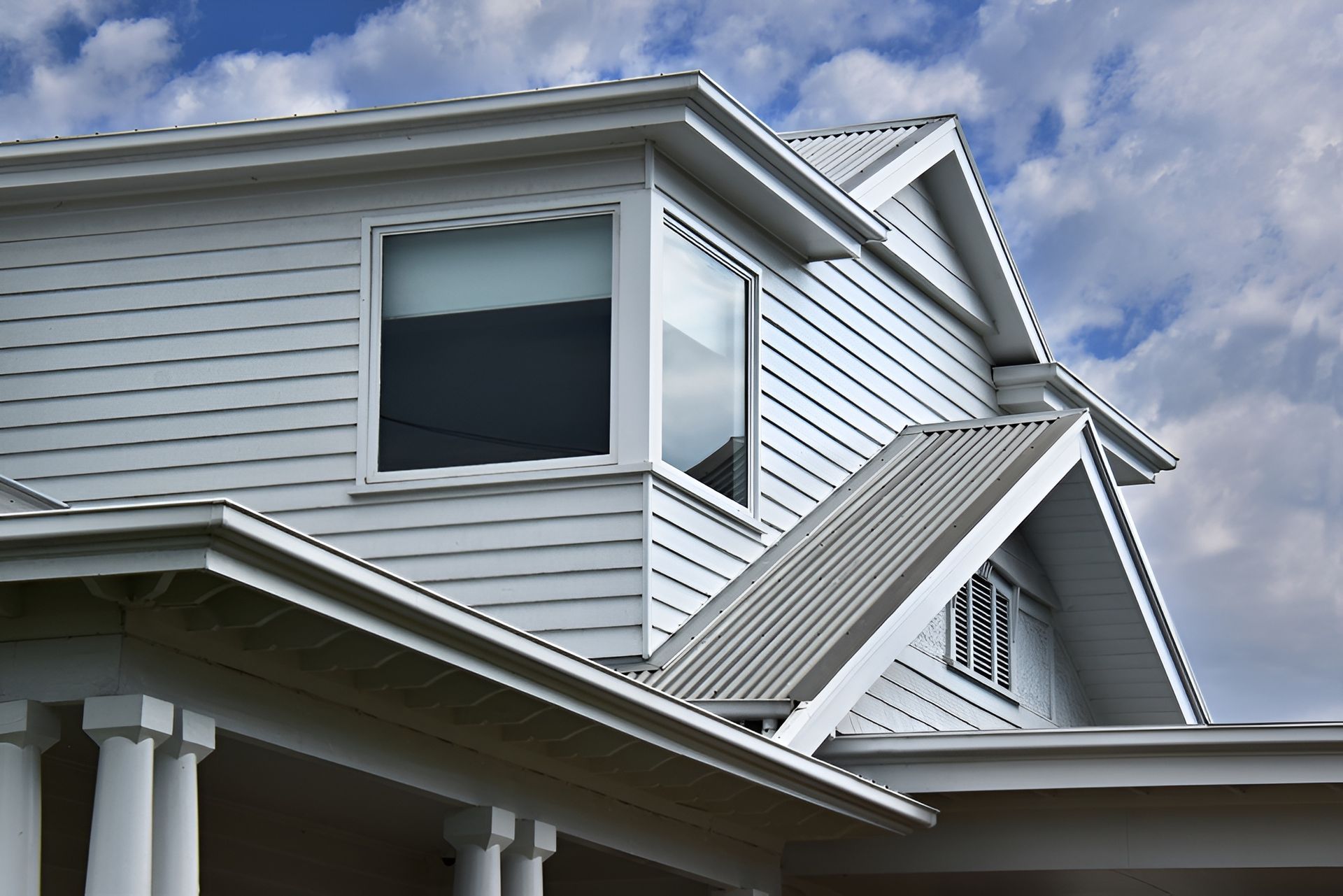White house exterior with a bay window, gabled roof, and porch columns against a cloudy sky.